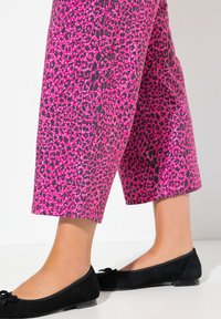 Fuchsiové kalhoty s leopardím vzorem, zkrácené a vyrobené z lehkého materiálu, doplněné černými plochými botami se zdobným detailem mašle.