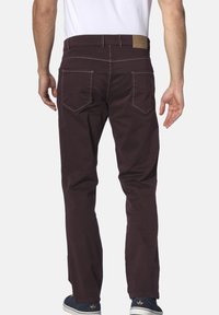 Burgundy pants with visible stitching, straight cut, two back pockets, and a tan leather label at the waist. Styled with navy shoes.