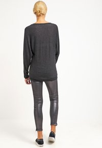 Suéter negro de punto con mangas largas, combinado con pantalones ajustados gris metálico y zapatos negros tipo slip-on. Textura suave y ajuste relajado.