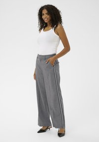 Sive široke hlače s crno-bijelim bočnim prugama, s dugmetom i džepovima, u kombinaciji s bijelim topom bez rukava i crnim potpeticama.