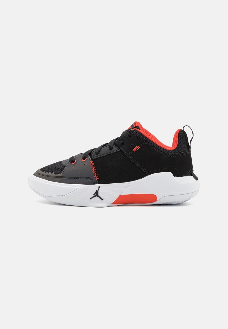 Chaussure de sport noire et rouge avec semelle blanche, logo Jordan, fermeture à lacets et col matelassé sur fond clair uni.