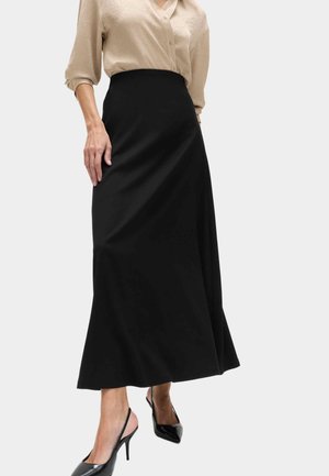 Frau trägt eine beige Bluse mit Knöpfen, in einen hoch taillierten schwarzen A-Linien-Midirock gesteckt und schwarze Slingback-Absätze.