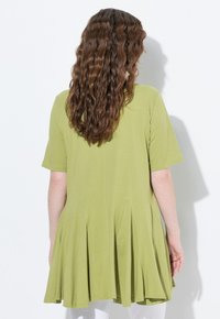 Groene tuniek met korte mouwen, een uitlopende zoom en plooidetails. Zachte stof, losse pasvorm en een rechte achterkant.