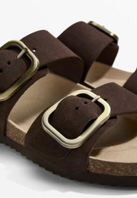 Barna velúr szandál két állítható pánttal, nagy ezüstszínű csatokkal és parafa talpbéléssel. Texturált gumitalp.