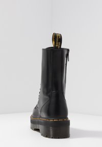 Schwarze Leder-Stiefelette mit dicker Plattformsohle, Schnürverschluss und gelbem Zugtab. Mit Nähten und einem Reißverschluss an der Seite.