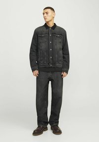 Jachetă din denim negru cu guler, nasturi pe față și două buzunare pe piept, asociată cu blugi negri cu croială lejeră și cizme negre.