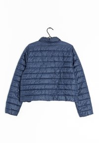 Blå vadderad jacka med oval mönster hängande på en svart galge, visad bakifrån mot en vit bakgrund.