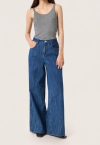 Kraťasy s širokými nohavicemi z modré denimu s vysokým pasem, předními kapsami a klasickým zapínáním na knoflík. V kombinaci s šedým topem bez rukávů.