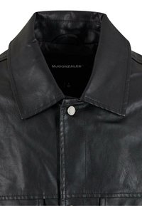 Schwarze Lederjacke mit breitem Kragen, silbernen Druckknöpfen und sichtbaren Steppnähten. Innenbranding ist in Weiß aufgedruckt.