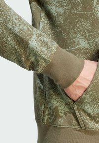 Grön hoodie i texturerat tyg med ett fläckigt mönster. Ärmarna är ribbade och det finns en framficka med öppning.