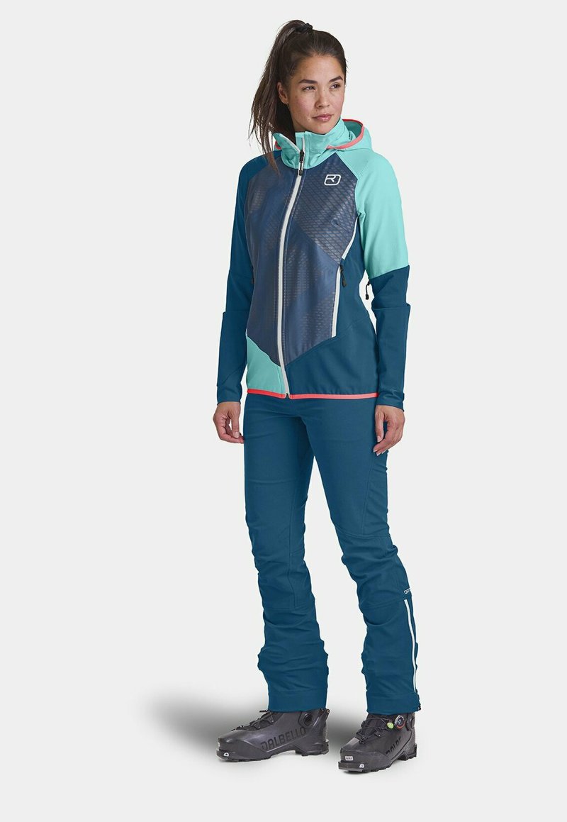 Ski jacket with a mix of dark blue and mint green panels; features a zip closure, textured fabric, and hood. Paired with matching blue ski pants.