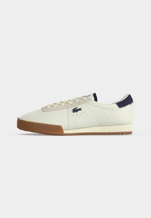 Weißer Low-Top-Sneaker mit beige-gummierter Sohle, beigen Schnürsenkeln, navyfarbener Fersenverstärkung und schwarzem Krokodil-Logo an der Seite.