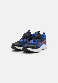 Chaussures de sport noires et bleues avec tige en maille, col rembourré et semelle extérieure en caoutchouc ; accentuées de détails rouges et dotées d'une sangle à boucle.
