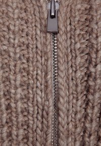 Maglione beige lavorato a maglia con una consistenza spessa, caratterizzato da una cerniera argentata al centro, che accentua il suo design informale.