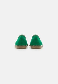 Scarpe in suede verde caratterizzate da un design liscio e arrotondato con una sottile rifinitura dorata e una suola beige chiaro. La vista posteriore mostra la forma elegante e la texture.