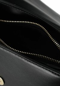 Interno di una borsa nera in pelle con una cerniera dorata, che mostra una texture liscia e un design semplice e funzionale.