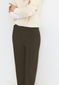 Pantaloni marroni su misura con una texture liscia, dotati di tasche e una vestibilità slim, abbinati a un maglione chiaro.