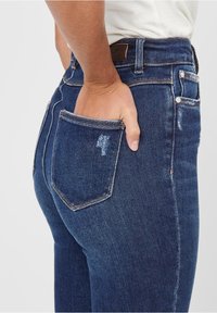 Pantalones vaqueros de denim azul oscuro con un diseño ajustado, que presentan un ligero desgaste, cinco bolsillos y una cinturilla clásica con detalles de costura.