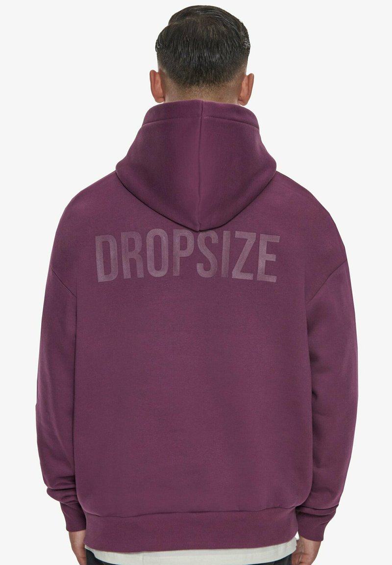 Lila huppari, jossa on suuri, vaaleanharmaa "DROPSIZE" -painatus selässä. Valmistettu pehmeästä kankaasta, jossa on rento siluetti ja säädettävä huppu.