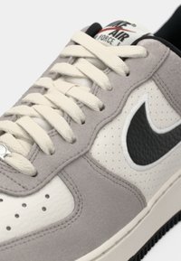 Szürke suede és fehér bőr sneaker perforált részletekkel és fekete Swoosh logóval. Krémszínű fűzők és gumitalp. Nike Air felirat a nyelvén.