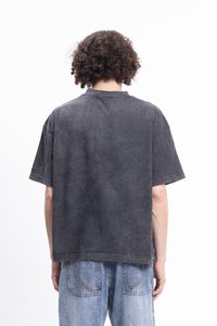 Černé oversized tričko s krátkým rukávem a opranou texturou, kulatým výstřihem a surovým lemem, spárované s světle modrými džíny s kontrastním šitím.