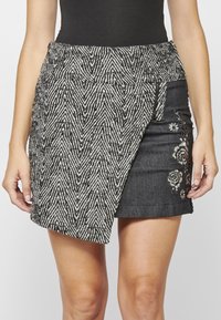 Jupe à motifs noir et blanc avec un design en chevrons texturé. Comprend un tissu en denim, une broderie florale et une coupe asymétrique.