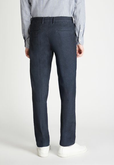 Pantalones azul marino de tejido suave, de corte ajustado, con dos bolsillos traseros y una textura suave, combinados con zapatillas blancas.
