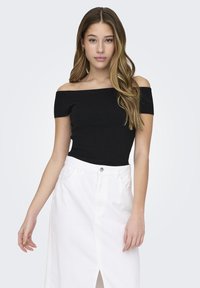 Melnas off-the-shoulder ribbed blūzes un baltas denima svārku komplekts, kuros ir priekšējais iegriezums un kabatas, uz gaiši pelēka fona.