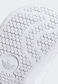 White rubber shoe sole featuring a textured pattern of small circles, with a logo embossed at the bottom center. Smooth, curved edge design.