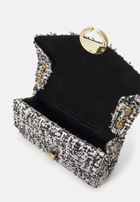 Sac à main en tweed noir et blanc avec un fermoir doré, des accents de chaîne, et un intérieur doux noir. Présente une forme rectangulaire structurée.
