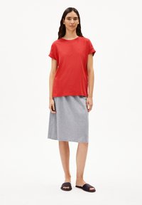 Rode katoenen T-shirt met korte mouwen, gecombineerd met een grijze jersey rok en zwarte slip-on sandalen. Eenvoudige, ontspannen pasvorm en basisontwerp.