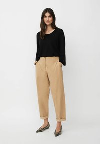 Maglietta nera a maniche lunghe, pantaloni color sabbia a sigaretta con orli arrotolati e ballerine a punta in stampa pitone. Texture liscia, design minimal.