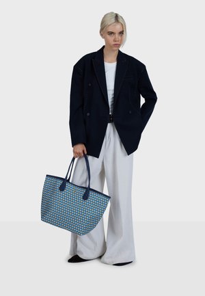 Navy plavi dvoredni blejzer s bijelim prošivima, uparen s bijelom košuljom i svijetlim hlačama visokog struka širokih nogavica. Plava torba za nošenje s uzorkom.