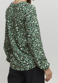 Blusa floreale verde e nera, con maniche lunghe, scollatura rotonda e una vestibilità morbida con dettagli raccolti sul retro.