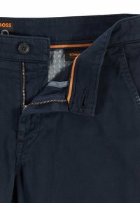 Pantaloni blu navy con chiusura a zip e bottone. Presentano dettagli arancioni, un motivo interno e tasche laterali. Realizzati in tessuto morbido.