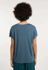 Top blu, a maniche corte, realizzato in tessuto a coste. Presenta un colletto rotondo e una vestibilità morbida che drappeggia leggermente sul retro.