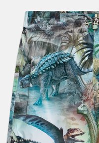 Shorts en tissu arborant un motif de dinosaures vif, présentant diverses espèces dans un paysage luxuriant et coloré avec des teintes de vert et de bleu.
