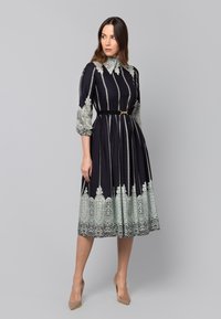 Granatowa sukienka w paski, z koronkowymi akcentami, wysokim kołnierzem, rękawami do trzech ćwiartek oraz wcięciem w talii. Posiada pełną spódnicę i pasek.