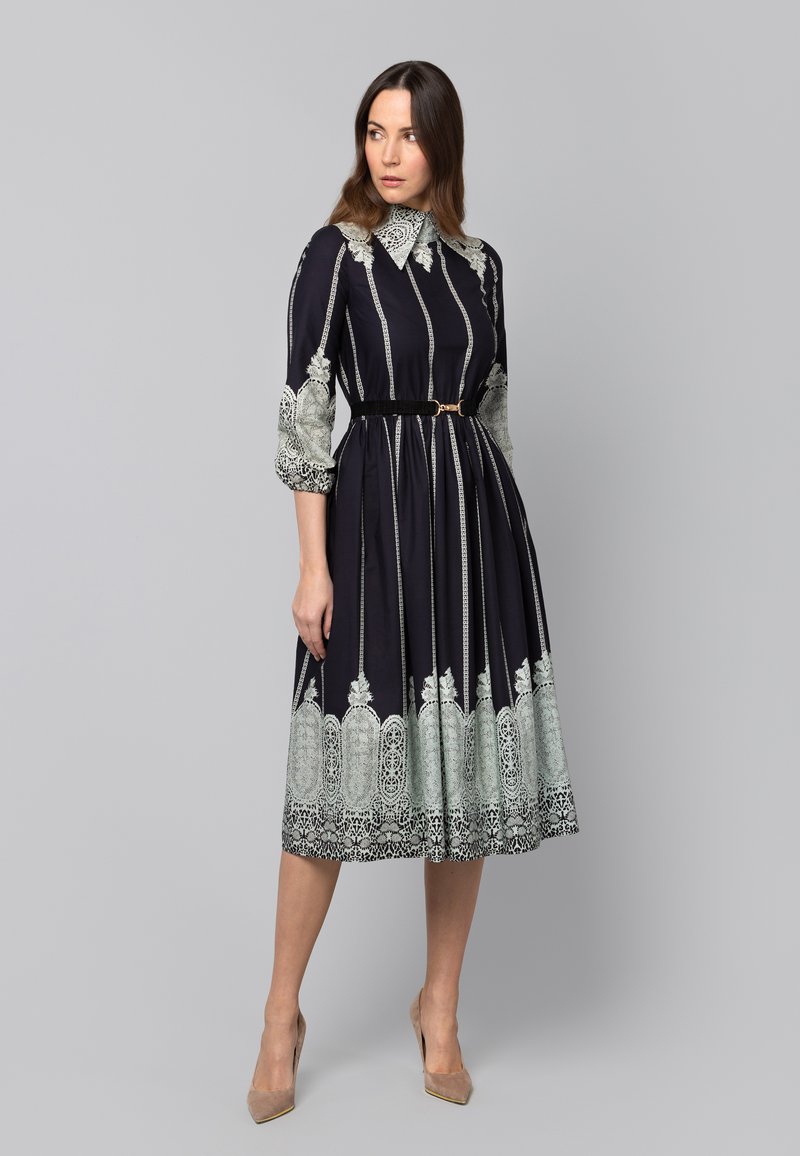 Granatowa sukienka w paski, z koronkowymi akcentami, wysokim kołnierzem, rękawami do trzech ćwiartek oraz wcięciem w talii. Posiada pełną spódnicę i pasek.