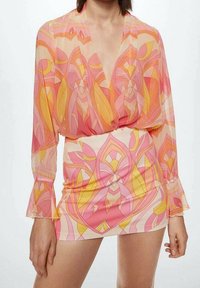 Robe à manches longues en tissu transparent présentant un motif géométrique rose et orange. Manches évasées et décolleté profond en V.