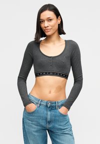 Γκρι cropped τοπ με μακριά μανίκια, στρογγυλή λαιμόκοψη και μαύρη ζώνη με λογότυπο, συνδυασμένο με ανοιχτού μπλε ψηλόμεσο τζιν παντελόνι.