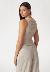 Haut sans manches beige clair avec un tissu froncé et une taille élastique. Associé à un pantalon cargo ample beige clair. Design épuré.