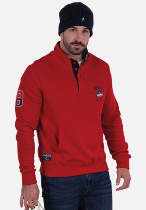 Sweatshirt rouge à finition texturée, avec un col marine, des boutons, le numéro 8 sur la manche gauche et une étiquette de marque à l'ourlet.