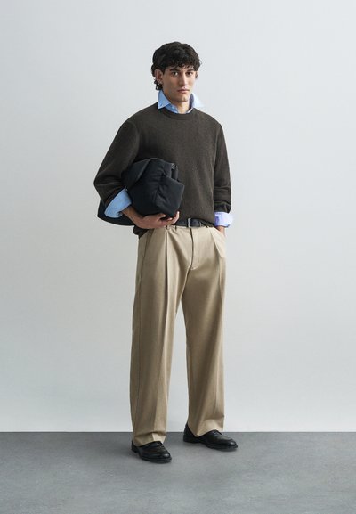 Σκούρος καφέ πλεκτός πουλόβερ, ανοιχτό μπλε πουκάμισο από κάτω, μπεζ παντελόνι φαρδιών ποδιών, μαύρη ζώνη, κρατώντας μια μαύρη τσάντα, μαύρα παπούτσια.