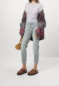 T-shirt lilas clair à col rond, cardigan tissé multicolore oversize, jeans bleu clair retroussés, sabots marron et un petit sac beige.