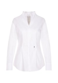 Blouse blanche à manches longues avec boutons, col mandarin et petite broderie noire en forme de fleur en bas à droite.