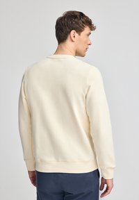 Felpa leggera color beige chiaro con collo a giro, polsini e orlo a costine, realizzata in tessuto morbido. Nessun motivo visibile. Design semplice e casual.