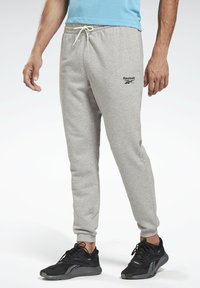 Pantalones de chándal grises de algodón con cintura elástica, cordón y logo de Reebok. Combinados con zapatillas deportivas negras.