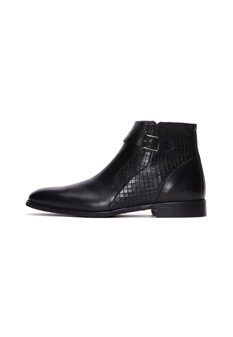 Botín de cuero negro con correa de hebilla lateral y panel texturizado, tacón bajo, punta lisa y estilo de deslizamiento.