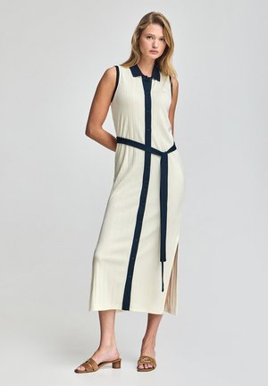 Ärmelloses, geripptes Midikleid in Creme mit navyblauen Akzenten, Vorderknöpfen, seitlichem Schlitz und passendem gebundenem Gürtel. Tragen mit sandfarbenen Absatzsandalen.